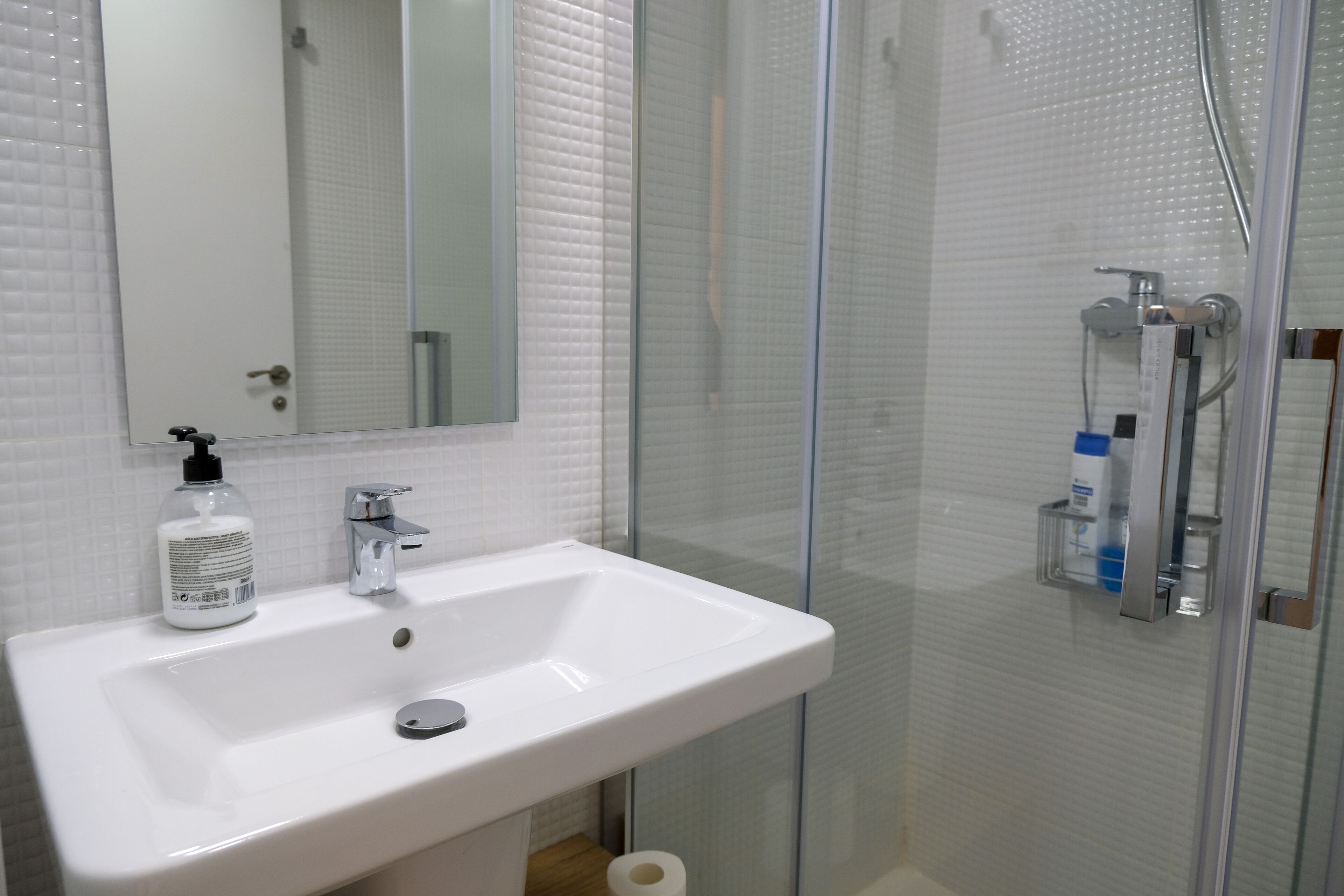 Un baño con un lavabo blanco, un espejo, cabina de ducha de vidrio y artículos de aseo en la pared.