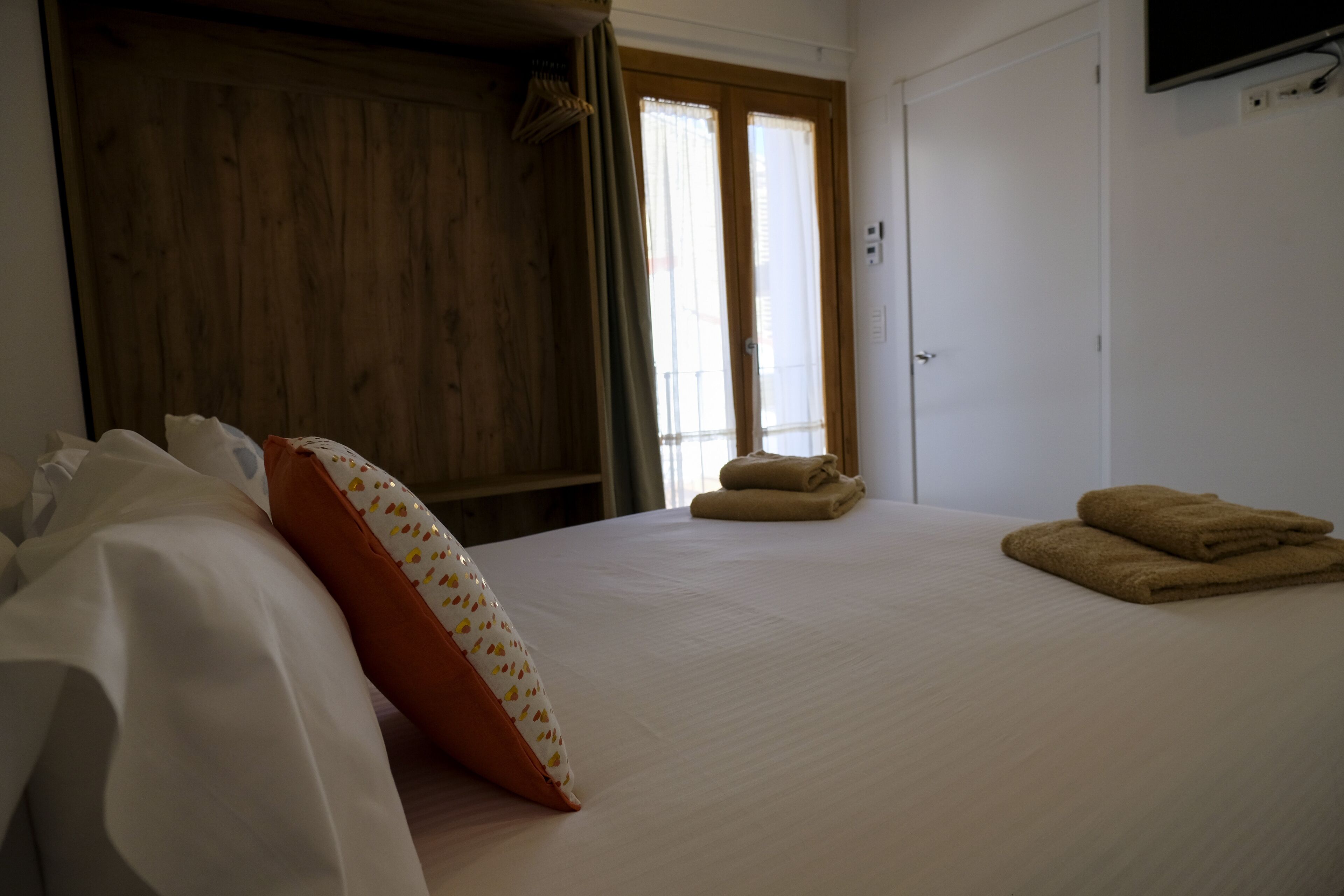 Un dormitorio con una cama, almohadas, un armario de madera y un televisor en la pared.