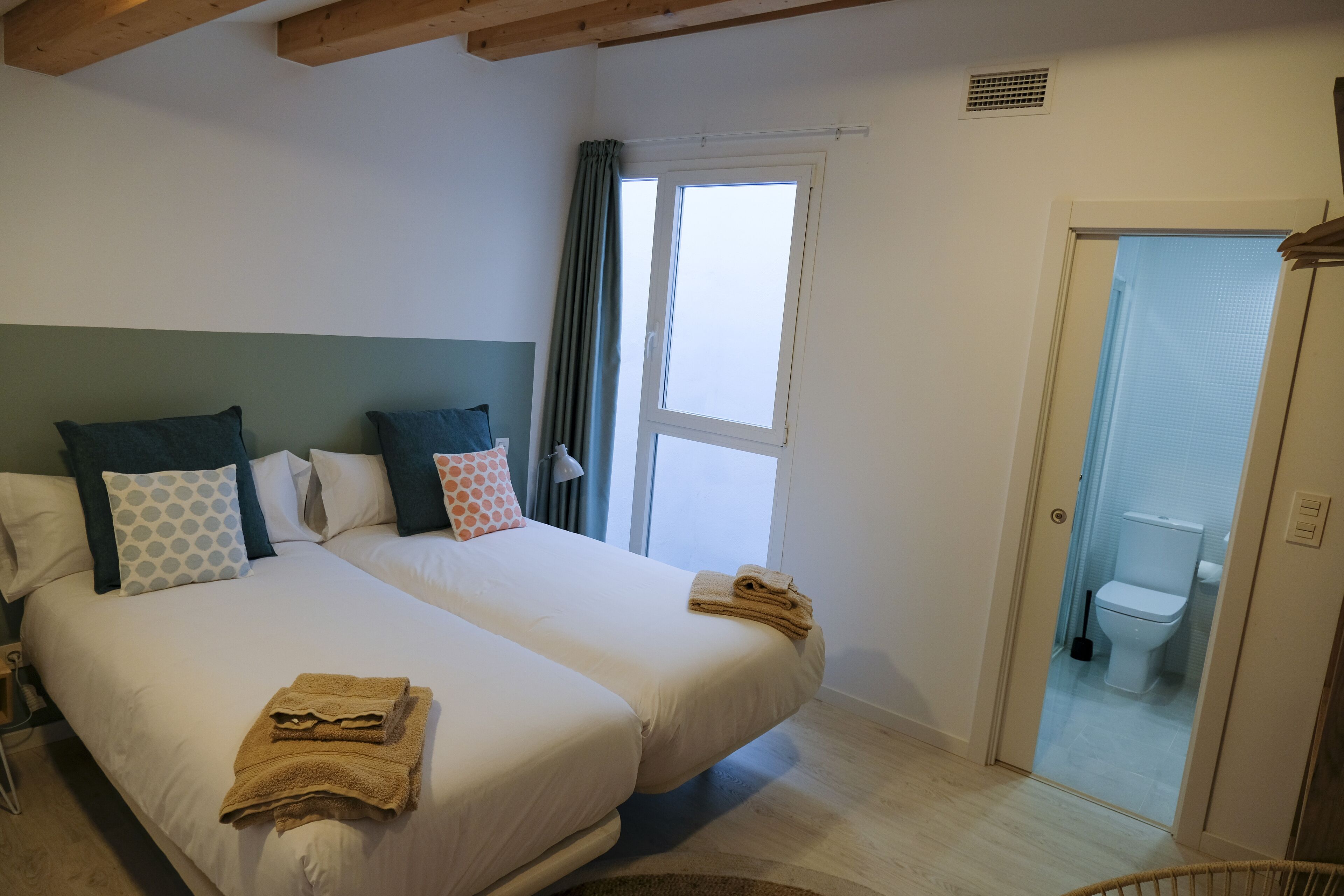 Habitació d'hotel amb dos llits, una finestra, una porta que dóna a un bany i un vàter visible.