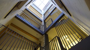 A multi-level interior with a central atrium, featuring a staircase with metal railings and a skylight above. - Silken Casa Platerias Siglo XV (Zaragoza)