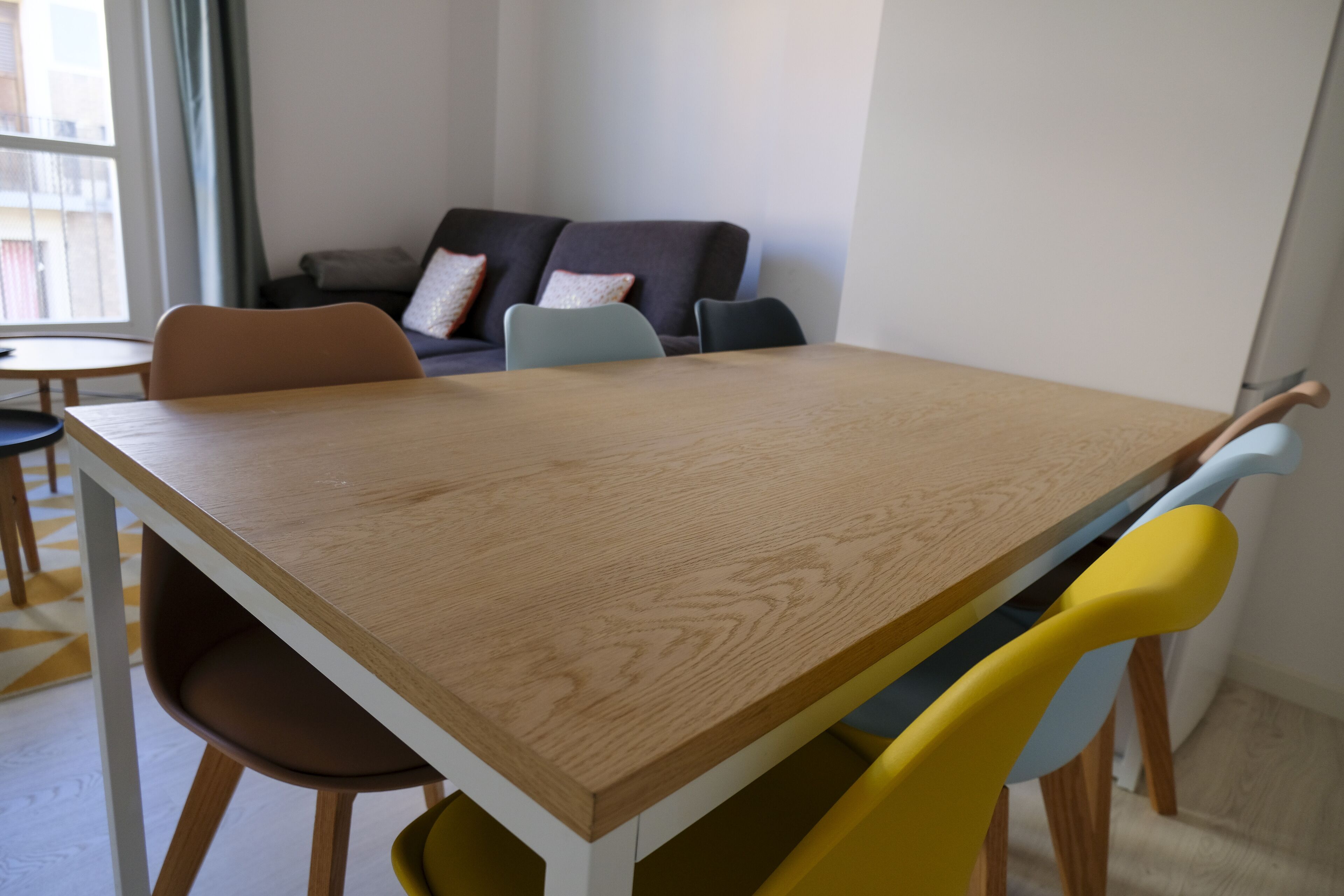 Ein Essbereich mit Holztisch und Stühlen, einer Couch mit Kissen und einem Fenster mit Vorhängen.