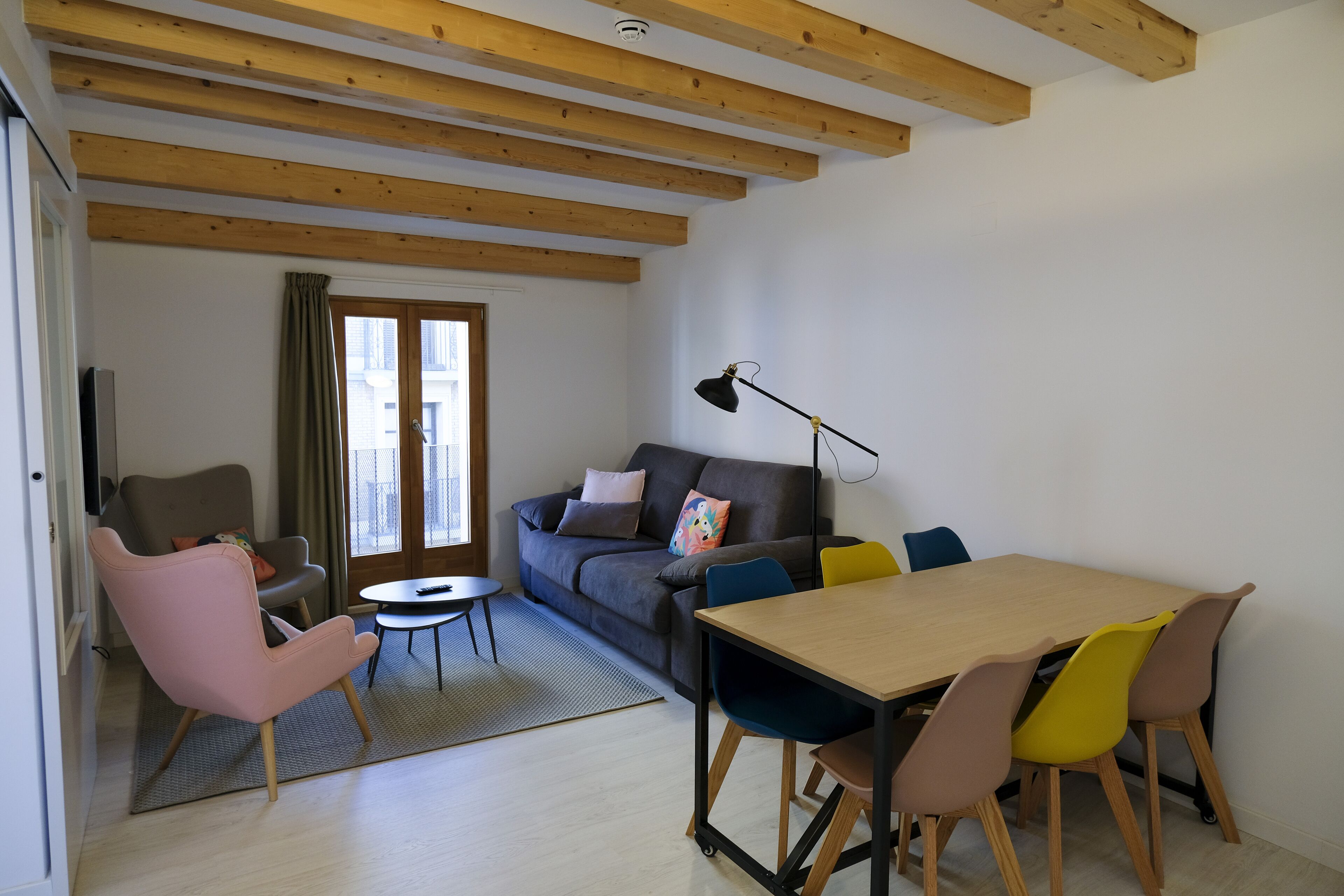 Una sala de estar moderna con un sofá, un sillón rosa, una mesa de comedor con sillas y una lámpara.