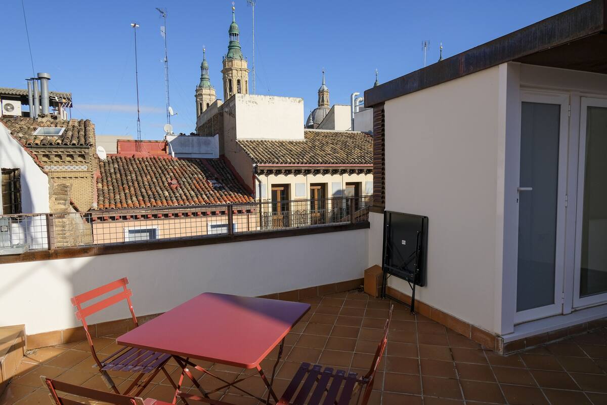 Una terraza en la azotea con mesa y sillas, un televisor y vistas de edificios históricos.