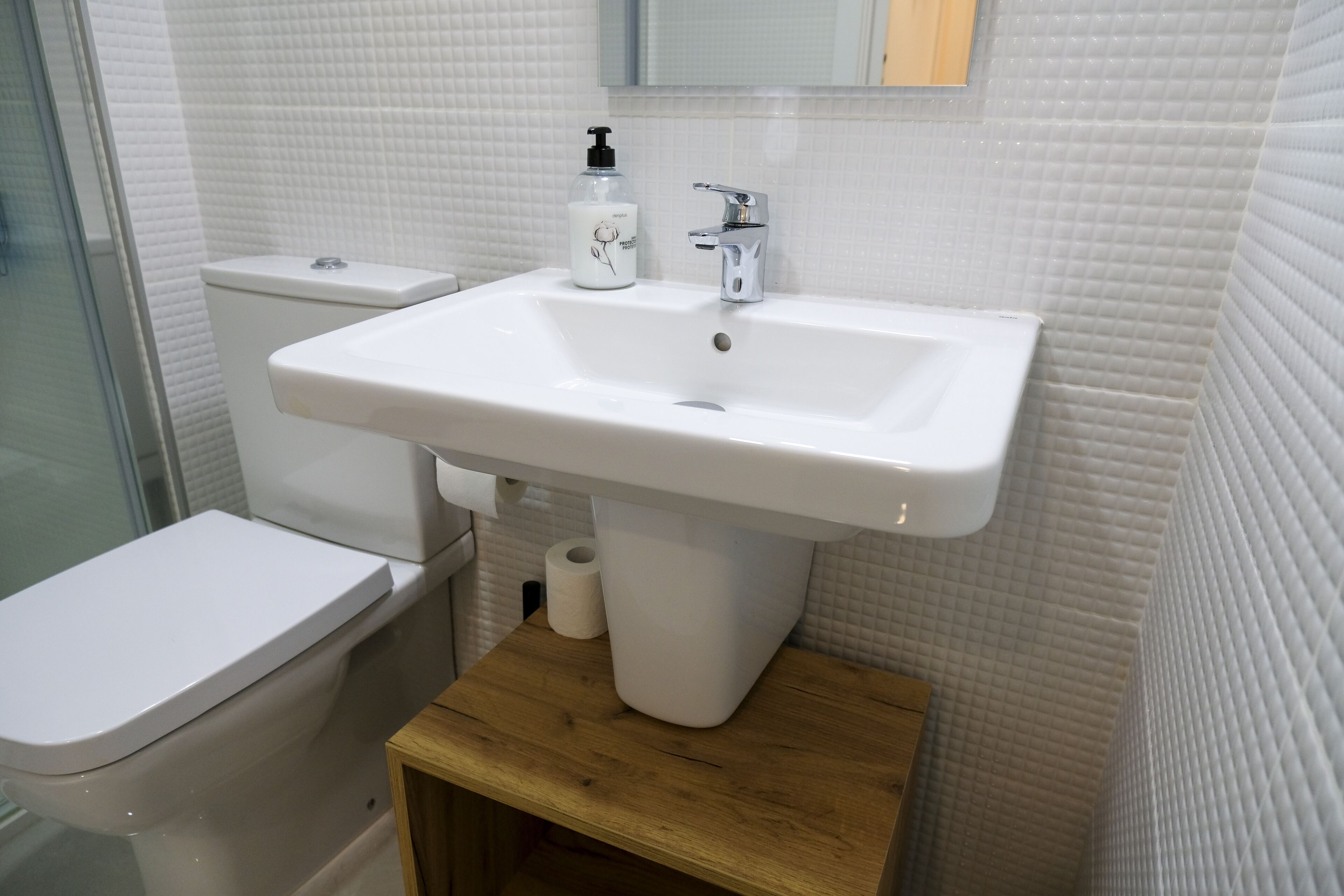 Un baño con lavamanos blanco, inodoro y tocador de madera.