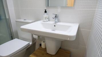 Un baño con lavamanos blanco, inodoro y tocador de madera.