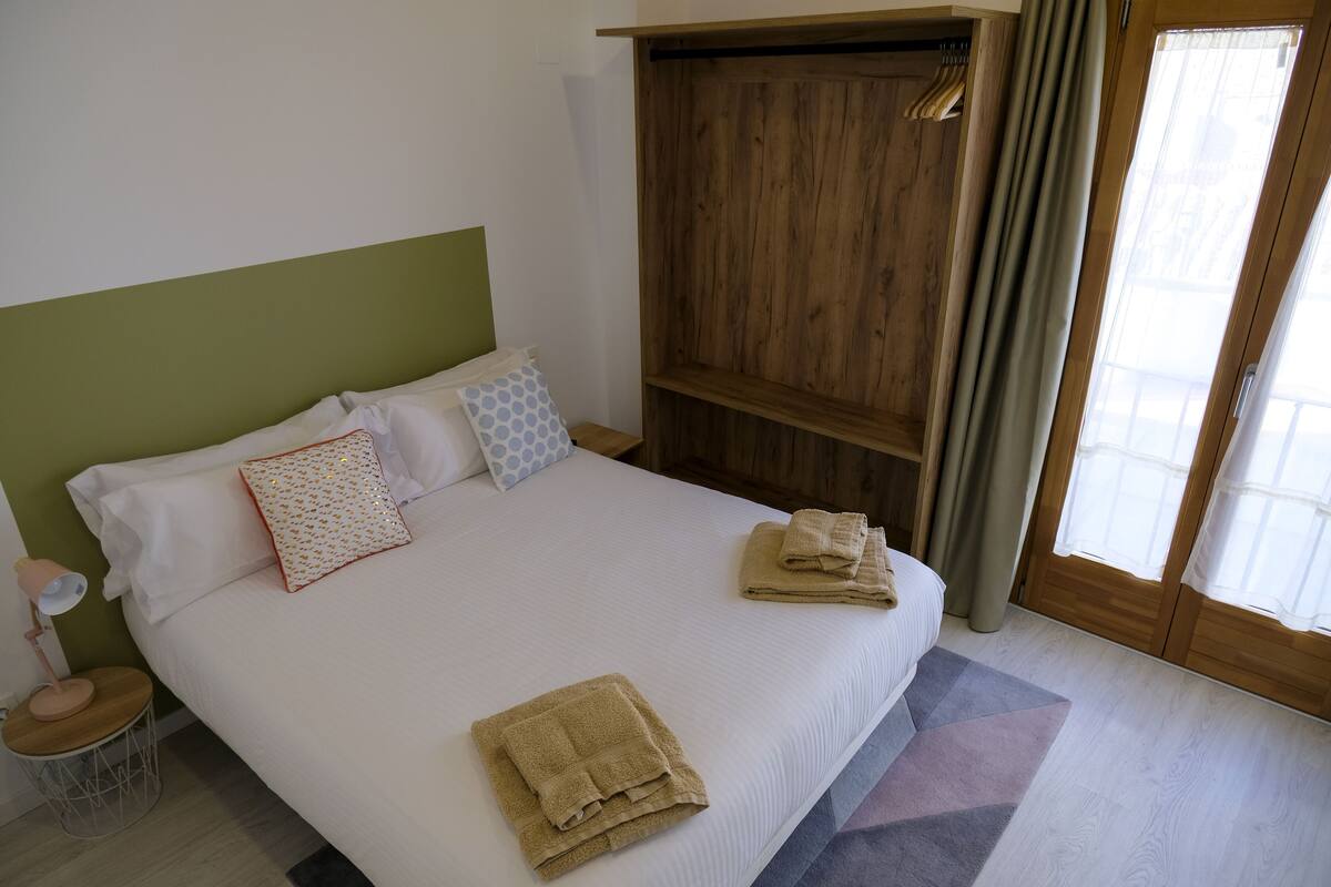 Una cama bien hecha con almohadas y toallas dobladas, una lámpara de noche y un armario de madera en una habitación de hotel.