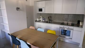 Une cuisine moderne avec des meubles blancs, un four à micro-ondes, un évier et une table à manger en bois, assortie de chaises colorées.