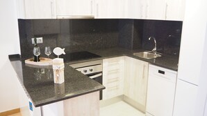 Een kleine keuken met witte kastjes, een zwart aanrecht, een roestvrijstalen spoelbak en een inbouwoven.