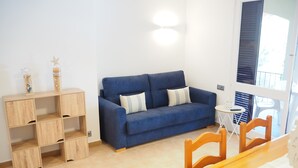 Een kamer met een blauwe bank, houten planken, een klein rond tafeltje en een eettafel met stoelen.