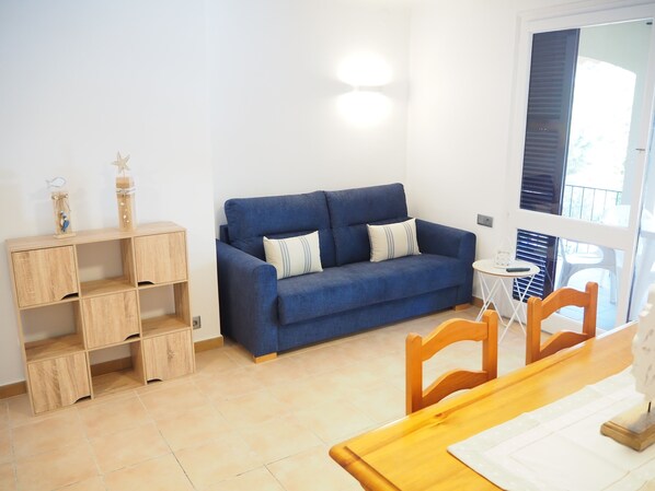 A room with a blue sofa, wooden shelves, a small round table, and a dining table with chairs.