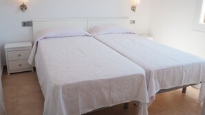 Een tweepersoonskamer met twee bedden, een nachtkastje en wandlampen.