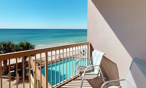 A balcony with a view of the ocean, a pool, and a chair.