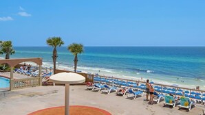 Blick auf einen Strand mit Pool, Liegestühlen und Palmen.