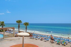A beachside view with a pool, lounge chairs, and palm trees. - Coastal Condo 707 | Beachfront! (Panama City)