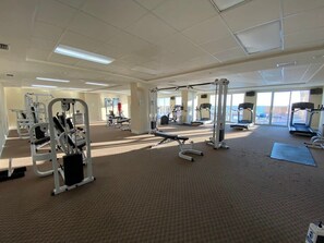 A gym with various exercise equipment, large windows, and a carpeted floor.
