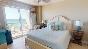 Ein Schlafzimmer mit einem Bett, zwei Nachttischen, einem Sessel, einem Balkon mit Meerblick und einer Glastür.