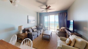 A living room with a sofa set, a coffee table, a TV, and a balcony with a view.