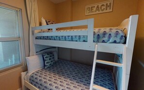 A bunk bed room with patterned bedding and a window with blinds.