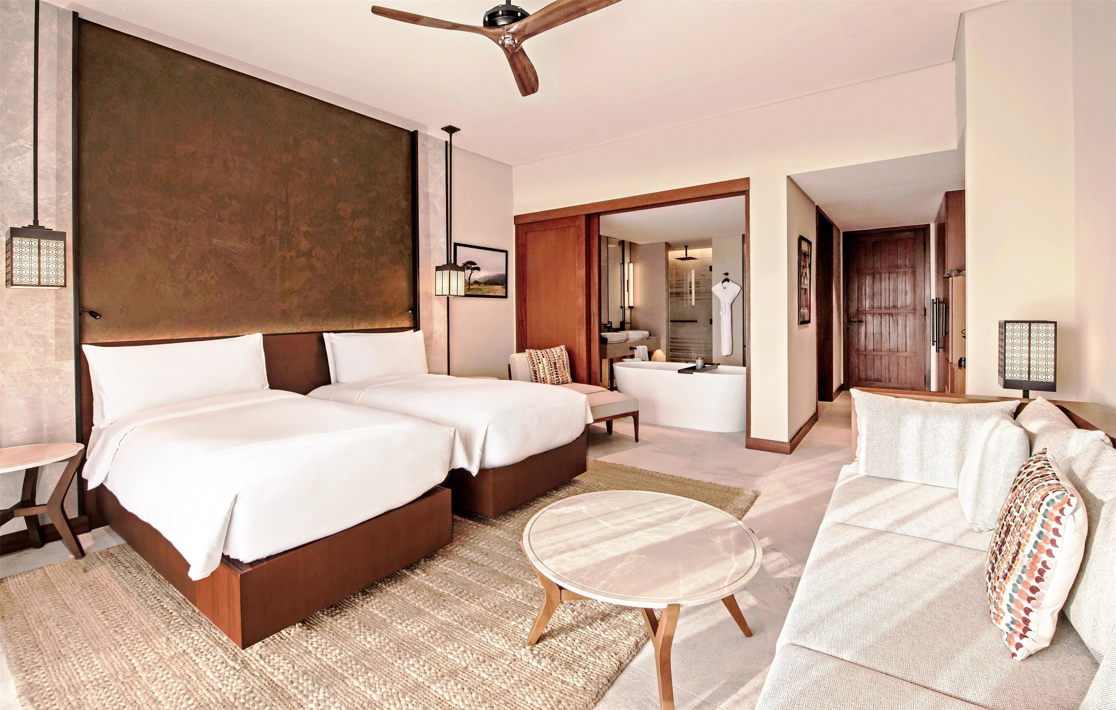 A modern hotel room with two large beds, a round coffee table, and a sofa.
