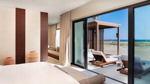 A hotel room with a large bed, a view of the beach, and a seating area with a wooden pergola. - Alila Hinu Bay (Mirbat)