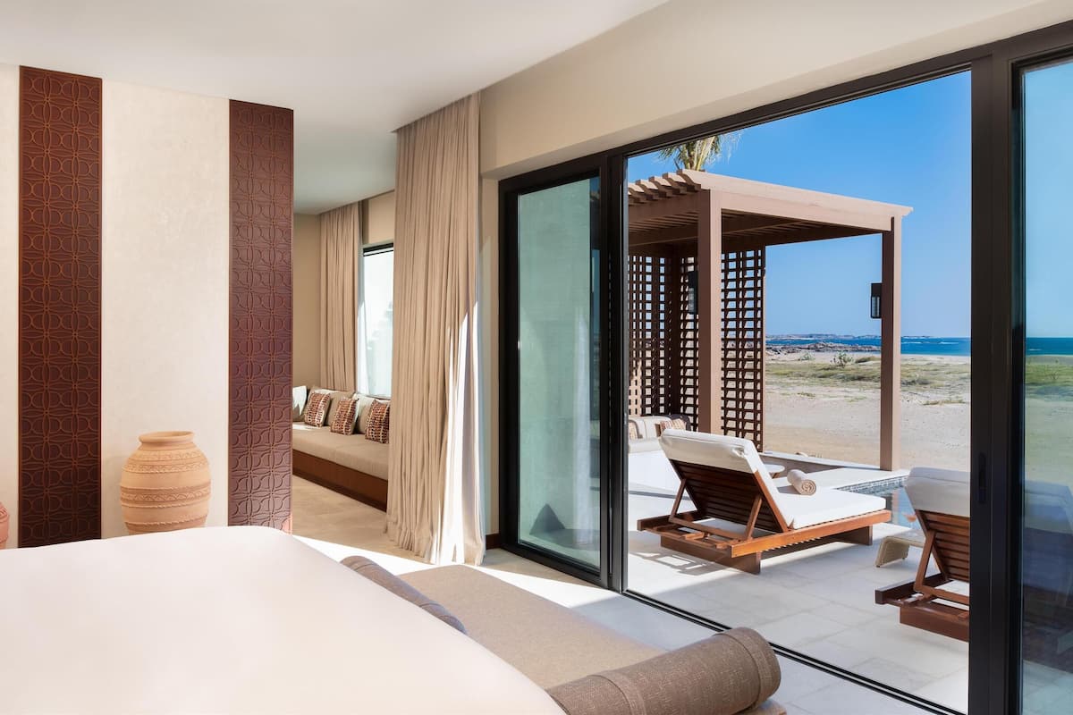 Une chambre d’hôtel dotée d’un grand lit, offrant une vue sur la plage, et comprenant un coin salon agrémenté d’une pergola en bois.