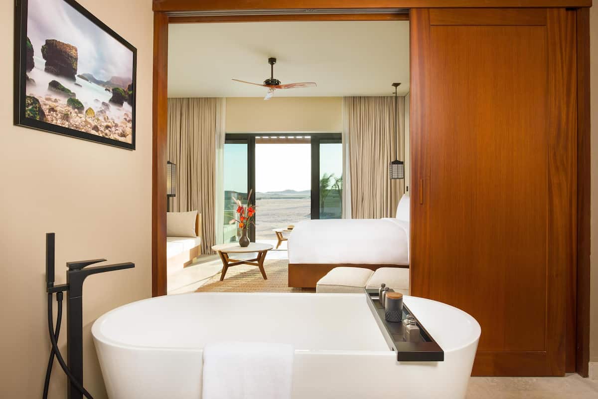Une chambre d’hôtel moderne dotée d’une grande baignoire, d’un canapé, d’une table à manger et offrant une vue sur la mer.