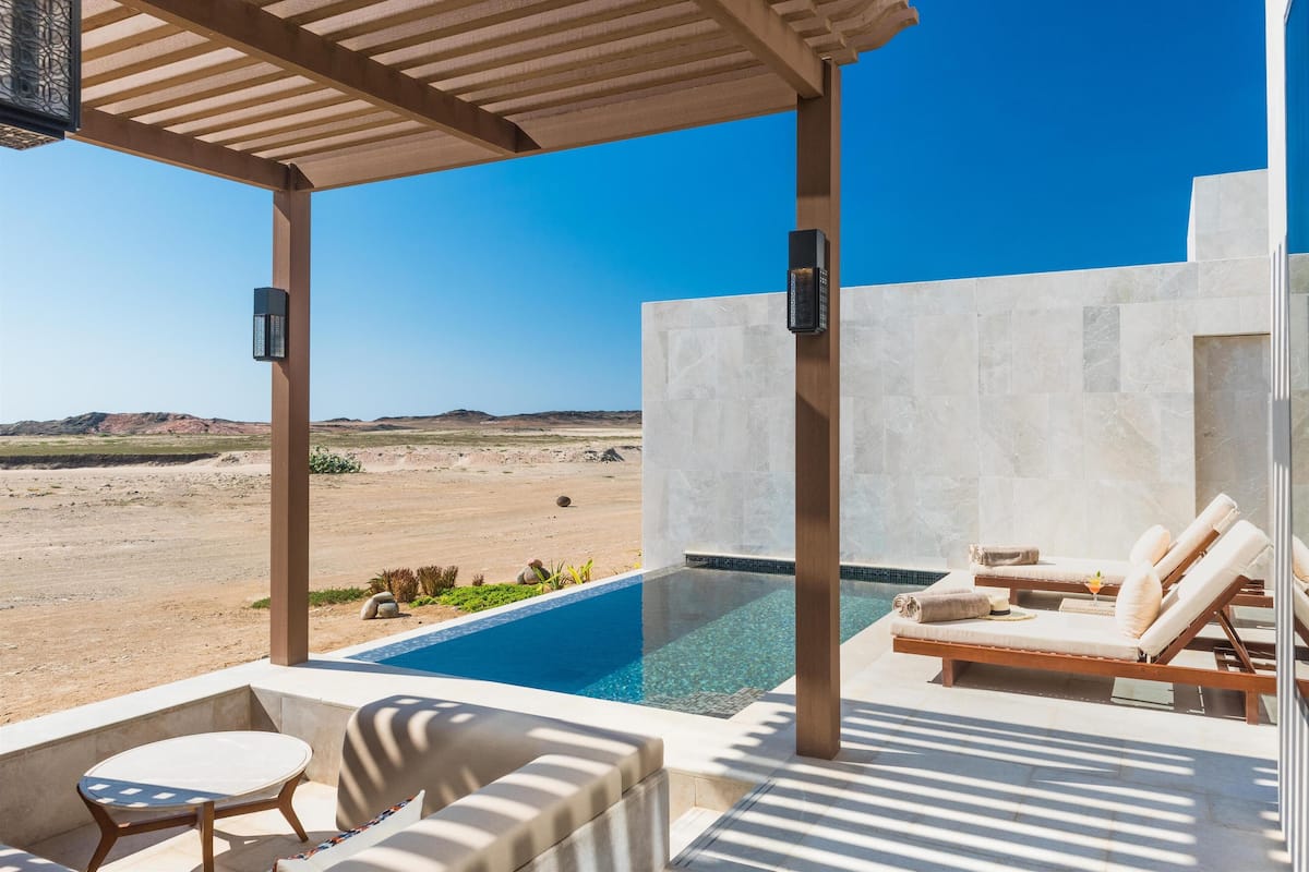 Un espace extérieur avec une piscine, des chaises longues et une table, offrant une vue sur un paysage désertique.