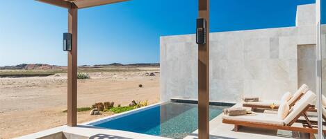 An outdoor pool area with lounge chairs and a table, overlooking a desert landscape.