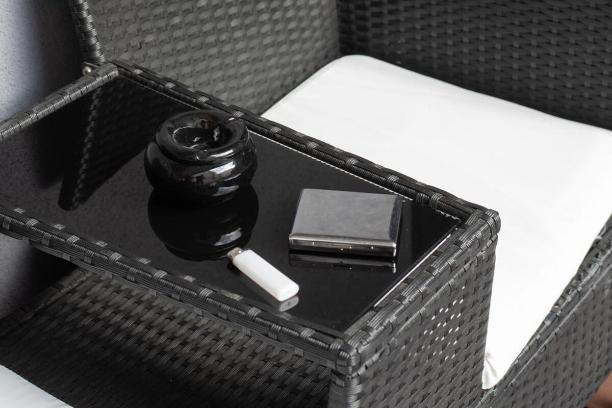 A wicker chair with a white cushion, a black tray with a black object and a white object on it, and a textured wall.