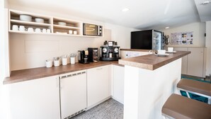 Una cocina moderna con armarios blancos, encimera de madera y electrodomésticos integrados, incluyendo una cafetera y un microondas.