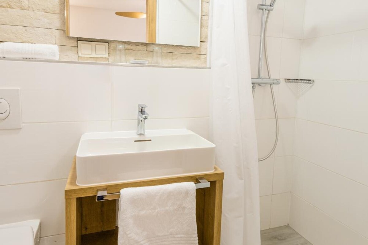 A modern bathroom with a wooden vanity, a white sink, a mirror, and a shower area.