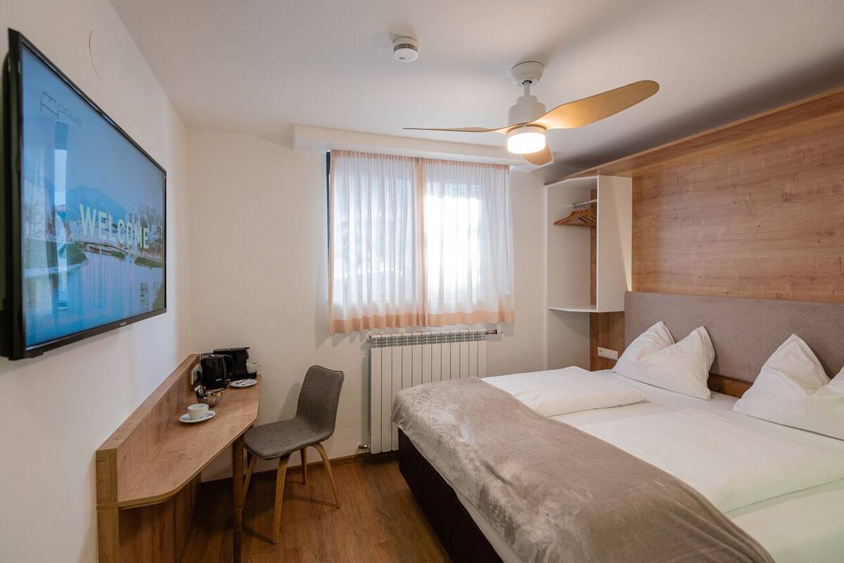 A hotel room with a bed, a desk with a chair, a television, and a window with curtains.