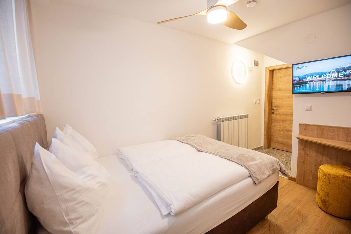 A hotel room with a bed, a television, a wooden door, and a radiator.