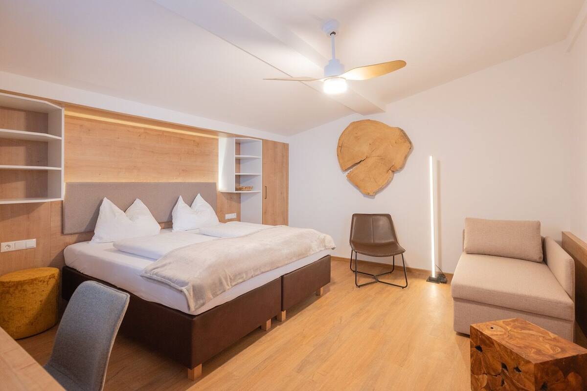 A modern bedroom with a bed, a chair, a sofa, and a wooden accent wall.