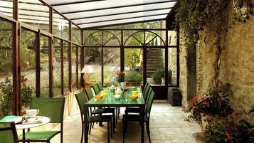 Ein Wintergarten mit Tisch für vier Personen, umgeben von Stühlen und Blick auf den Garten.