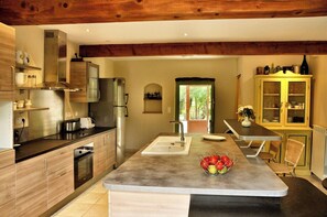 Eine moderne Küche mit Holzschränken, Edelstahlgeräten, einer zentralen Kochinsel mit Spüle und einem Essbereich mit Tisch und Stühlen.
