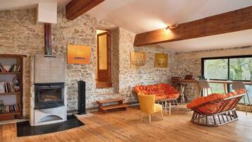 Ein gemütliches Zimmer mit Steinwand, Kamin, Holzbalken und einem großen Fenster.