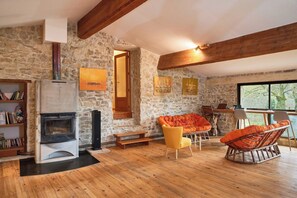 Ein gemütliches Zimmer mit Steinwand, Kamin, Holzbalken und einem großen Fenster.