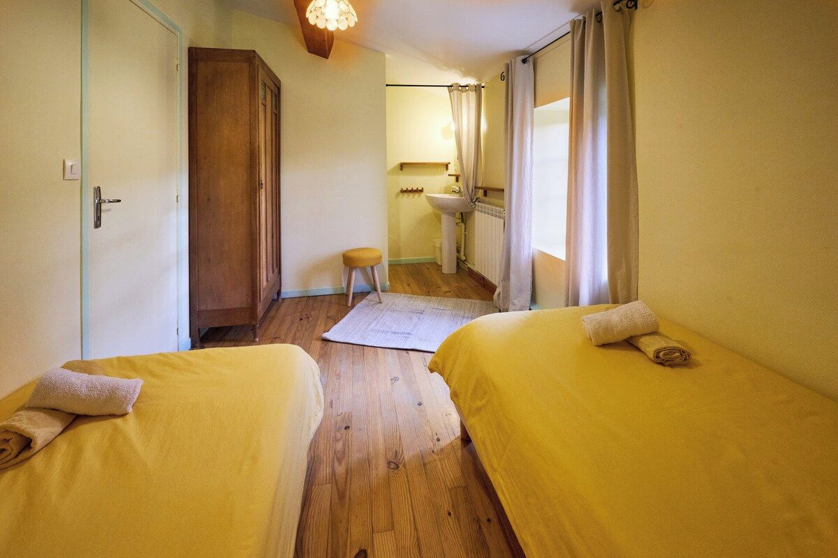 Une pièce avec deux lits, un plancher en bois, un petit tabouret, un lavabo et un miroir.