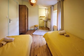 A room with two beds, a wooden floor, a small stool, a sink, and a mirror.