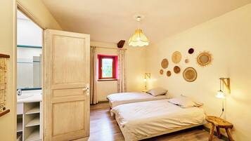 Une chambre avec deux lits, une porte en bois, une fenêtre avec des rideaux rouges et des éléments de décoration murale.
