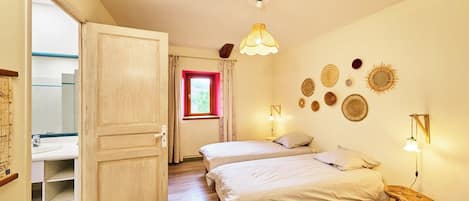 Un dormitorio con dos camas, una puerta de madera, una ventana con cortinas rojas y adornos en la pared.