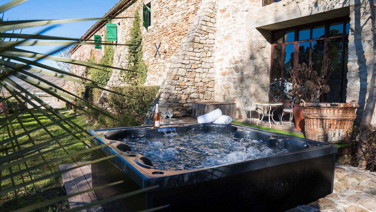Een jacuzzi in een tuin met stenen muren en een tafel met stoelen.