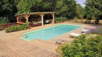Une terrasse en bois avec une piscine, un espace salon extérieur et une zone abritée.
