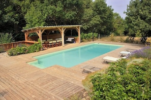 A wooden deck with a swimming pool, outdoor seating, and a covered area.