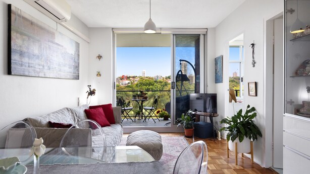 A modern living room with a glass dining table, a sofa with red cushions, and a balcony with a view of the city. - BAYSIDE BLISS - PRIVATE & TRANQUIL WITH VIEWS, AIR CONDITIONING AND LIFT (Rushcutters Bay)