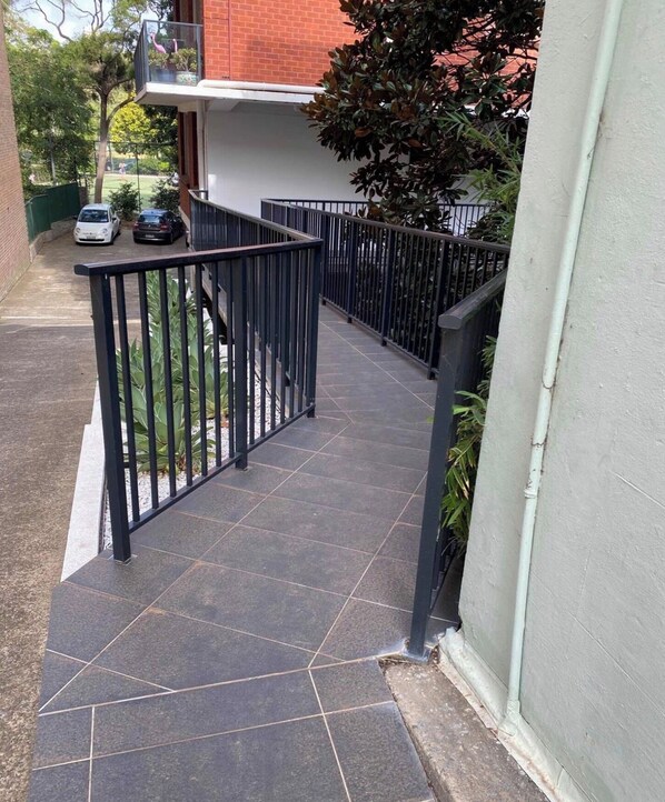 A residential building with a tiled walkway, a metal railing, and a brick wall.
