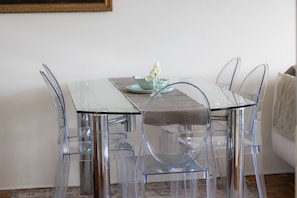 Una mesa de comedor de vidrio transparente con sillas, un adorno pequeño sobre la mesa y una pared lisa al fondo.