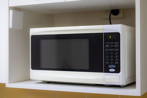 Un horno microondas blanco con pantalla digital y panel de control, ubicado en un estante de cocina.