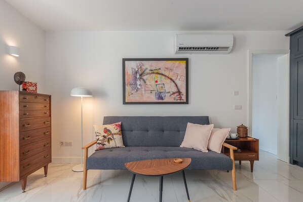 Una sala moderna con un sofá gris, una mesita de madera, una lámpara de pie y un cuadro en la pared.